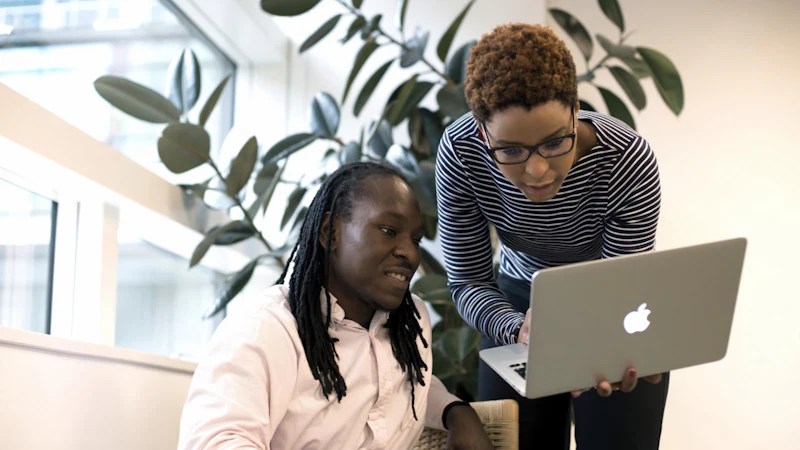 A mentor guiding someone through a task on a laptop